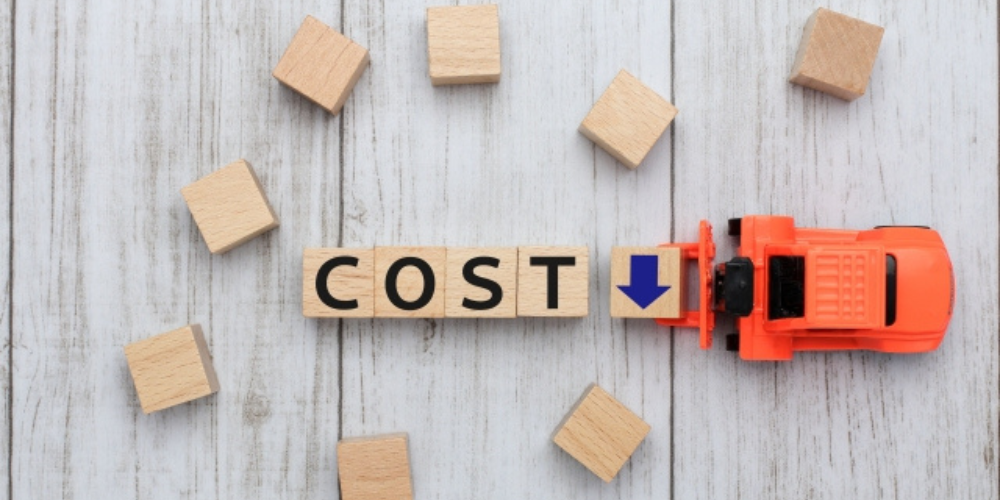 木製ブロックで「COST」と書かれ、横に青い下向き矢印があるブロックをオレンジ色のミニカーが押している様子