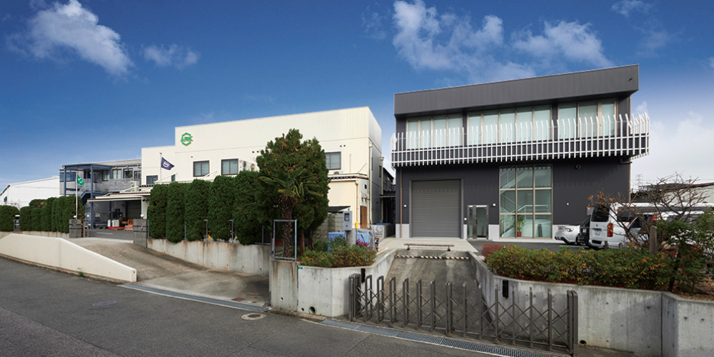 株式会社荒木製作所本社・工場外観—白い工場棟と黒いオフィス棟を並べた企業施設を道路側から撮影