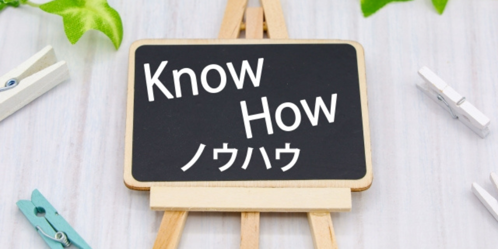 黒いミニボードに「Know How ノウハウ」と書かれた表示。背景にクリップや葉っぱ