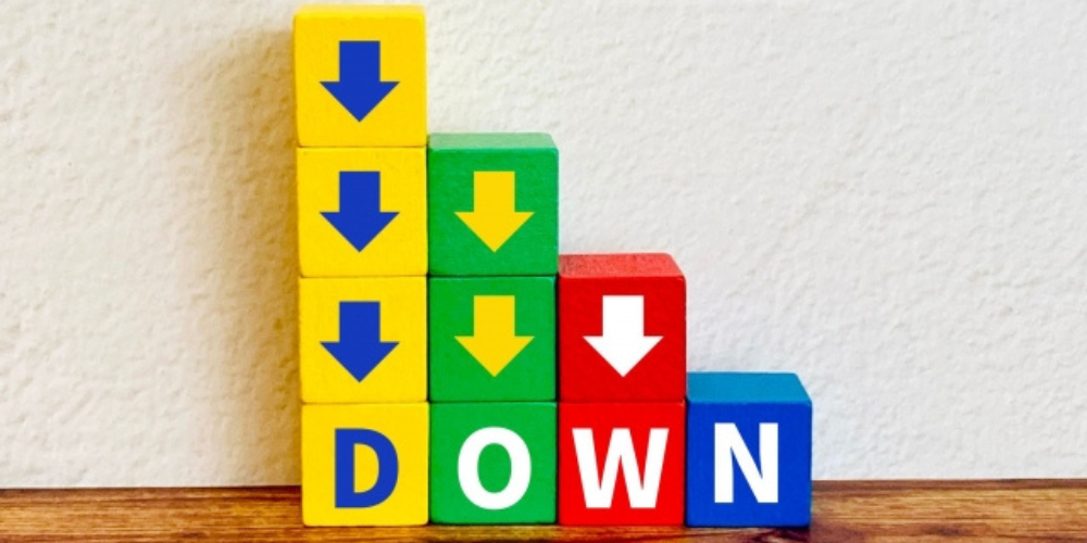カラフルな積み木に青と白の下向き矢印と「DOWN」の文字が並び、コスト削減のイメージを示している