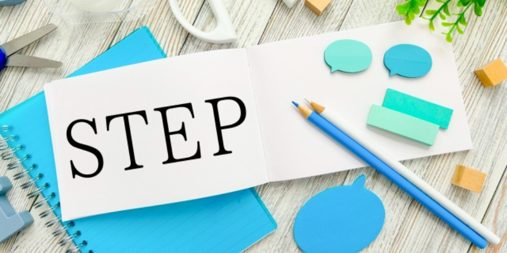 ノートに「STEP」と書かれ、周囲に文房具や吹き出し型の付箋が置かれた作業スペース