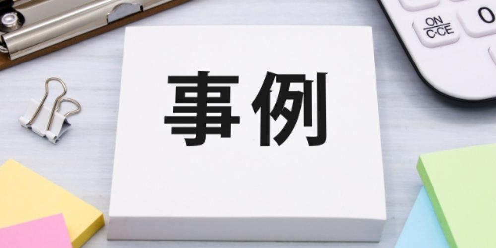 「事例」と書かれた白いメモ用紙の周りに、文房具や電卓が配置されたデスク上のイメージ。