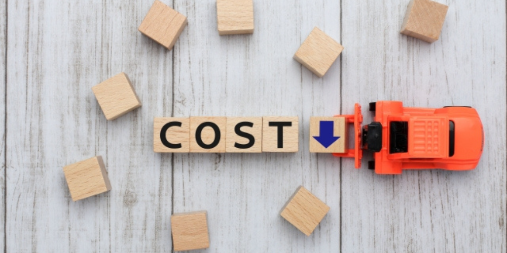 木製ブロックで作られた「COST」と矢印、コスト削減を表すイメージ