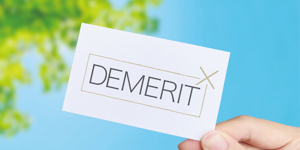 手にした名刺サイズのカードに「DEMERIT」文字と × 印を配したデメリット提示イメージ
