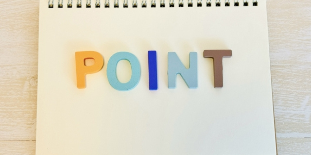白いノートの上にカラフルなアルファベットで「POINT」と並べられた明るい構図。