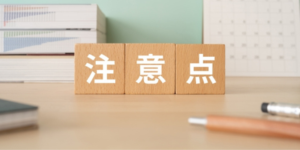  木製ブロックに「注意点」と書かれた文字が並び、背景には本やカレンダー、ペンが置かれている。