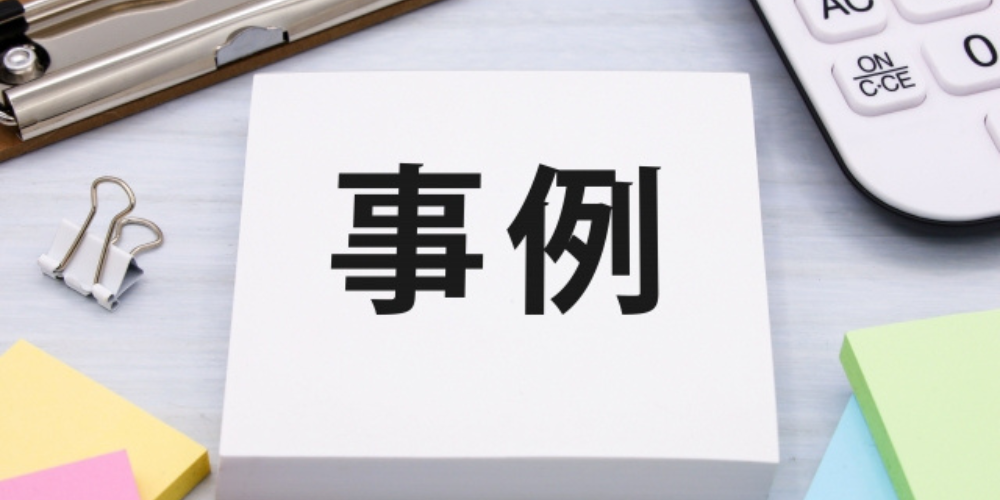 「事例」と書かれた白いメモ用紙の周りに文房具や電卓が配置されたデスク上のイメージ。