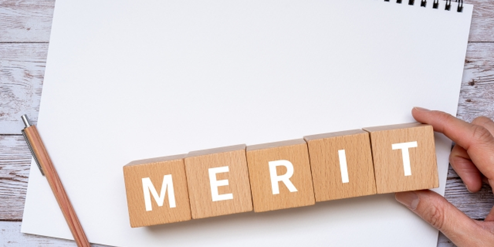 「ノートの上に並べられた『MERIT』の木製ブロック、メリットや利点を説明するイメージ」