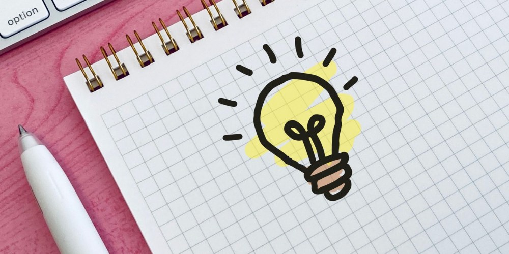 閃きを表す電球のイラストが描かれたノートとペン