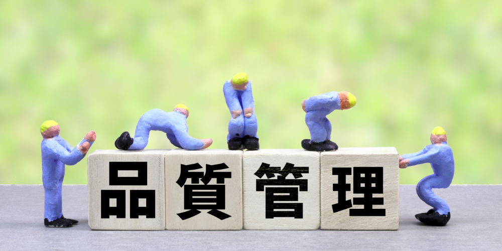 「品質管理」と書かれたブロックの上で作業するミニチュア作業員の模型