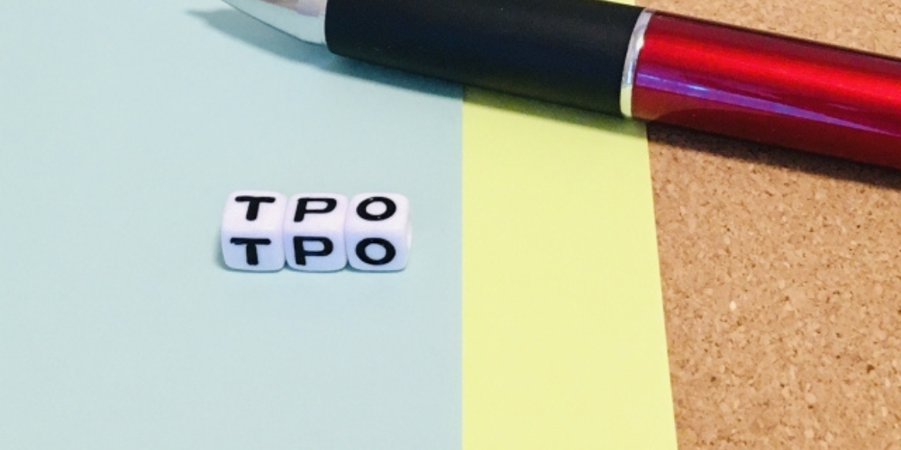 水色と黄色の用紙の上に「TPO」のキューブが置かれ、右上には赤いボールペンが添えられている構成