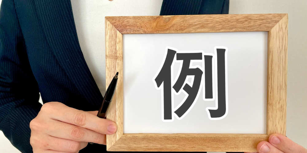 木製フレームに書かれた「例」の文字を持つスーツ姿の人物