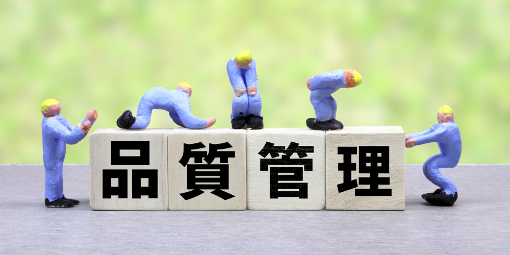 木製ブロックに「品質管理」と書かれ、作業員の人形が並んでいる様子