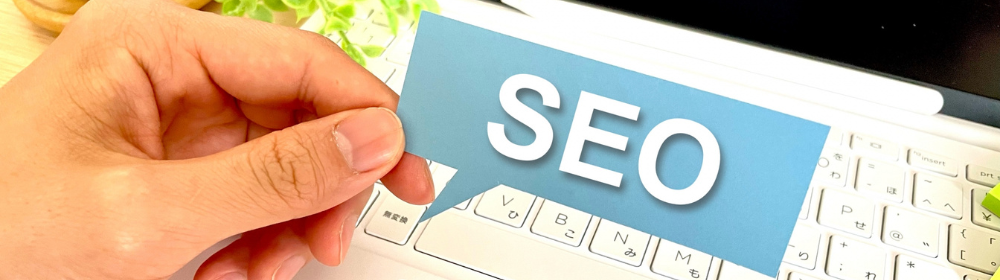 SEOと書かれた青いカードを持つ手と白いノートパソコンのキーボード
