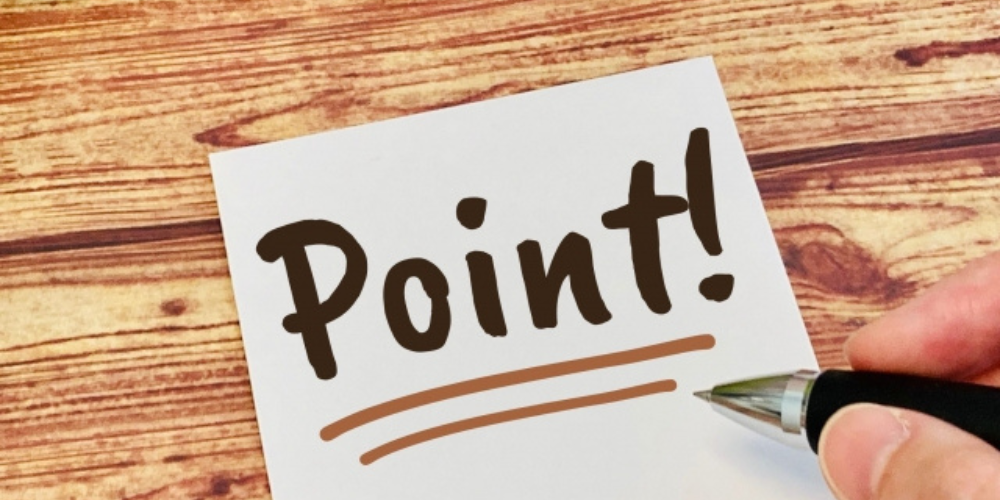 木目のテーブルの上に「Point!」と書かれたメモと、右手に持たれたペンの構成