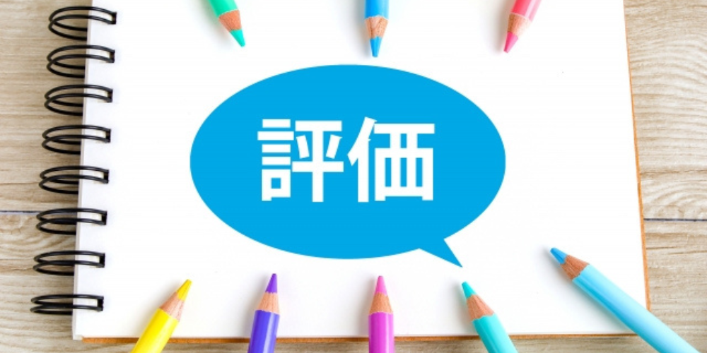 ノートの上に「評価」と書かれた吹き出しと色とりどりの色鉛筆が並ぶ画像