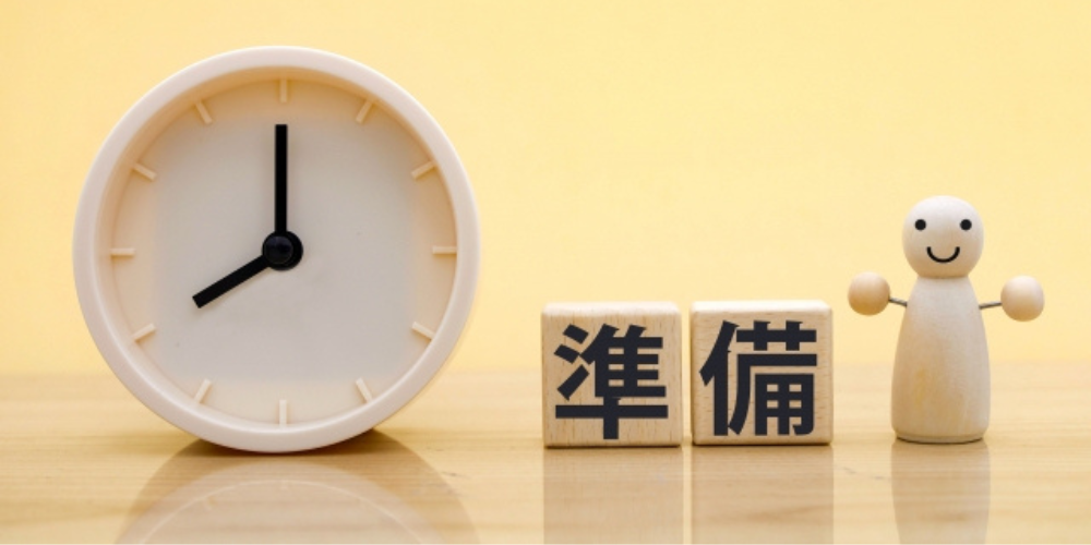 時計と「準備」と書かれたブロックの横に笑顔の木製人形が立っている