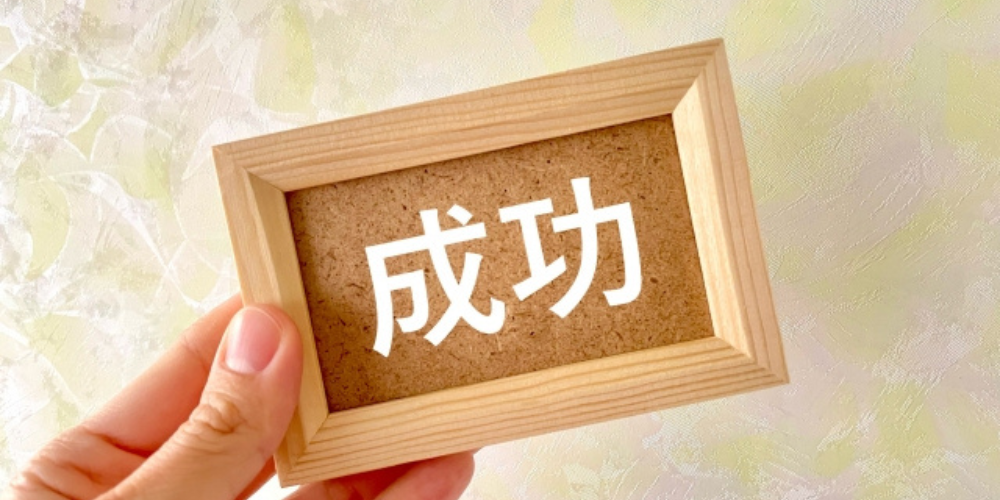 手で持たれた木製フレームに「成功」の文字が白く記されている