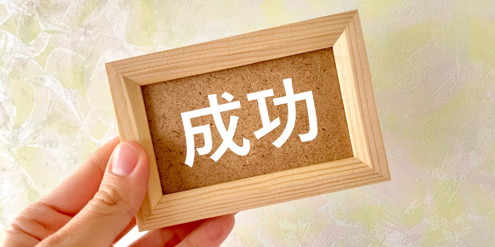 「成功」と書かれた木枠のボードを手に持っているイメージ