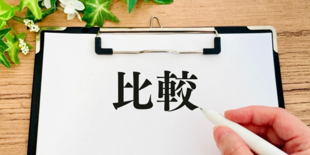 クリップボードの紙に「比較」の文字、ペンを持った手と植物の装飾