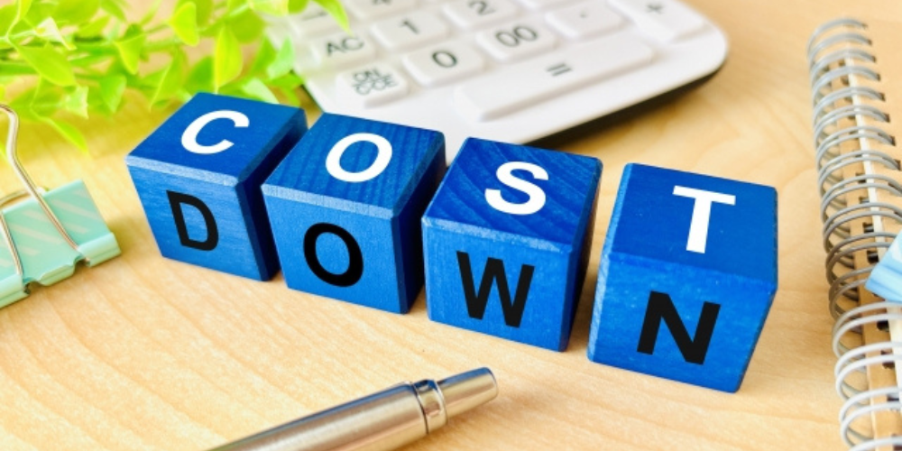 青いブロックに「COST DOWN」と書かれた文字と文房具のあるデスク