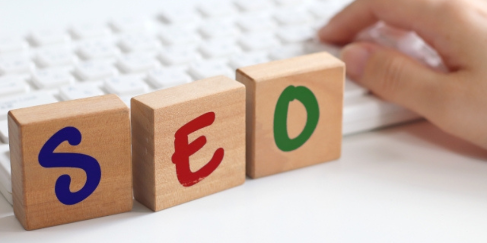 木製ブロックに赤青緑で「SEO」と描かれたキーボード前のシーン