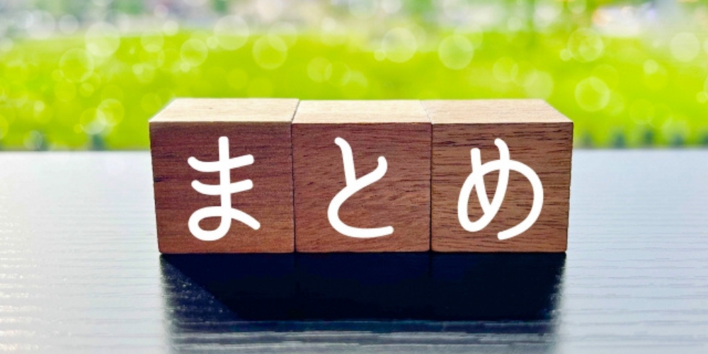 木のブロックに白文字で「まとめ」と書かれ、背景は緑のぼかし風景