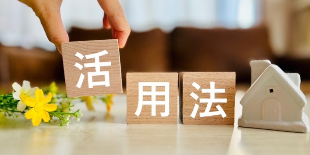 木製ブロックに「活用法」と書かれた文字と、隣にある家の模型や黄色の花が並ぶ生活感のある構成