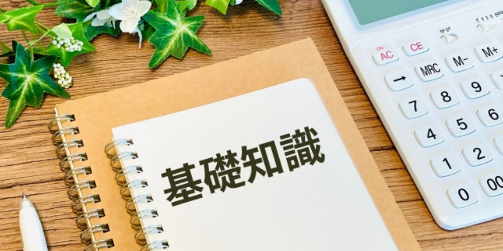 木目調の背景にノートと電卓、「基礎知識」と書かれた文字と観葉植物をあしらった構成