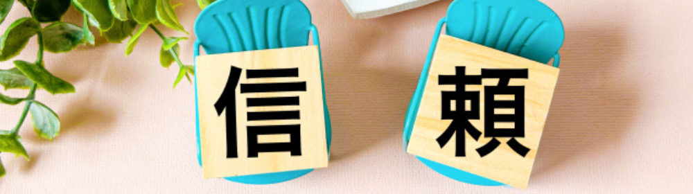 ピンクの背景に置かれた青い椅子の上に「信」「頼」と書かれた木片が並べられた画像