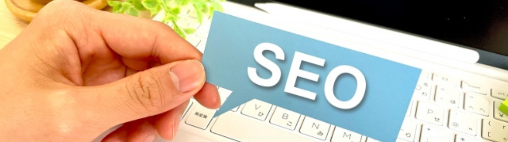 手に持った「SEO」のカードとノートパソコンのキーボード