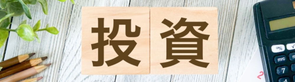 木目調の背景に「投資」と書かれた木製ブロック、横には電卓や鉛筆が並ぶ