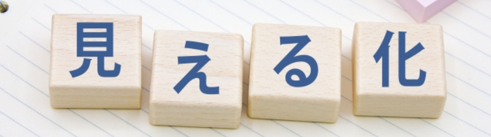 「見える化」と書かれた木製ブロックがノート上に並ぶ