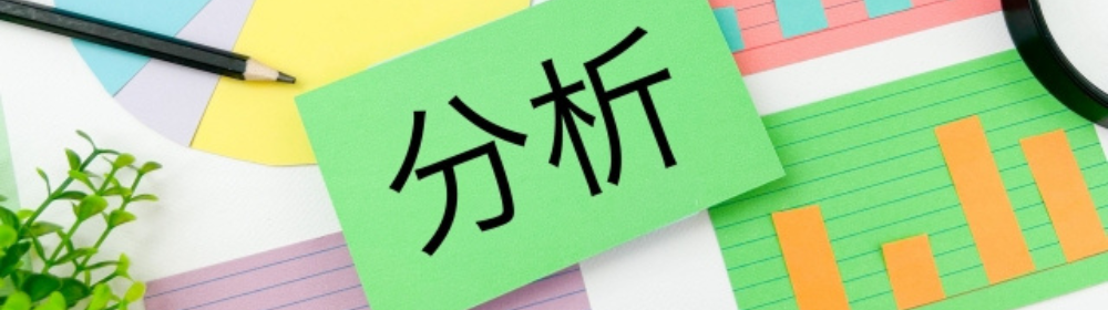 グラフや棒グラフの上に「分析」と書かれた緑のカード、鉛筆と植物が添えられた構成