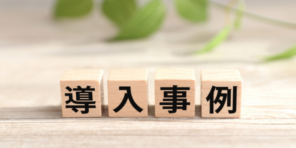木のブロックに「導入事例」の文字が書かれ、背景には観葉植物の葉がぼかされたナチュラルな雰囲気
