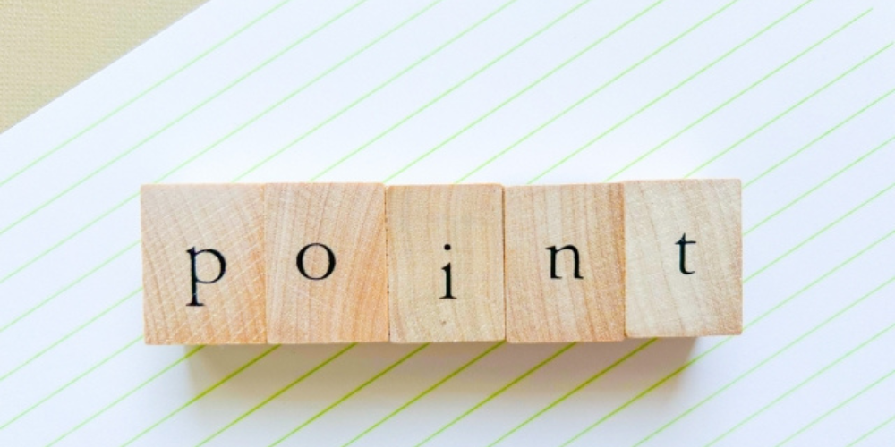 斜めのノートの上に「point」の文字が書かれた木製ブロックが並べられたシンプルな構成